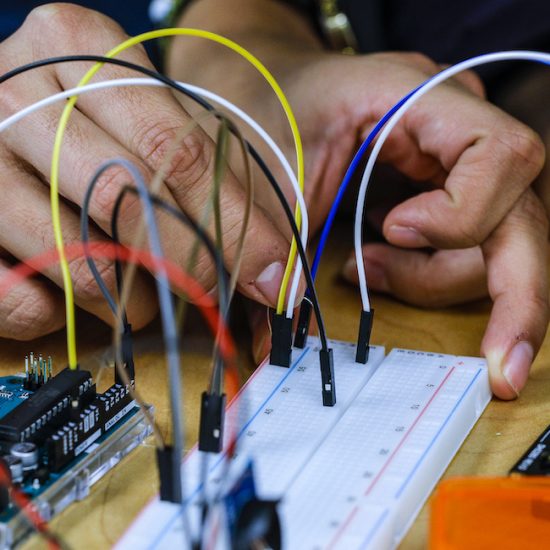 A student's hands manipulate a circuit board in a tinkering project